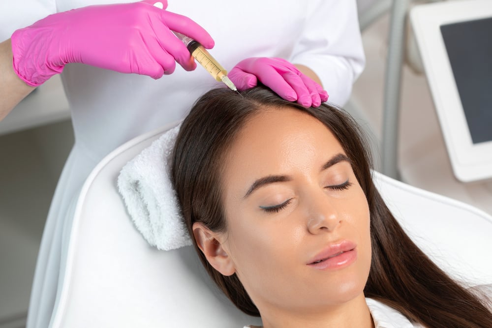 Cosmetologist does prp therapy against hair loss and anti-dandruff of a beautiful brunette woman in a beauty salon. Aesthetic cosmetology concept, hair treatment.